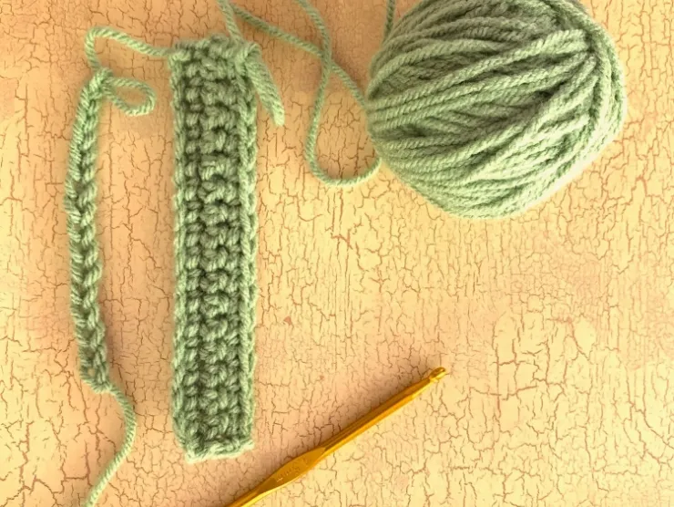 Photo of a green ball of yarn attached to a small piece of crochet
