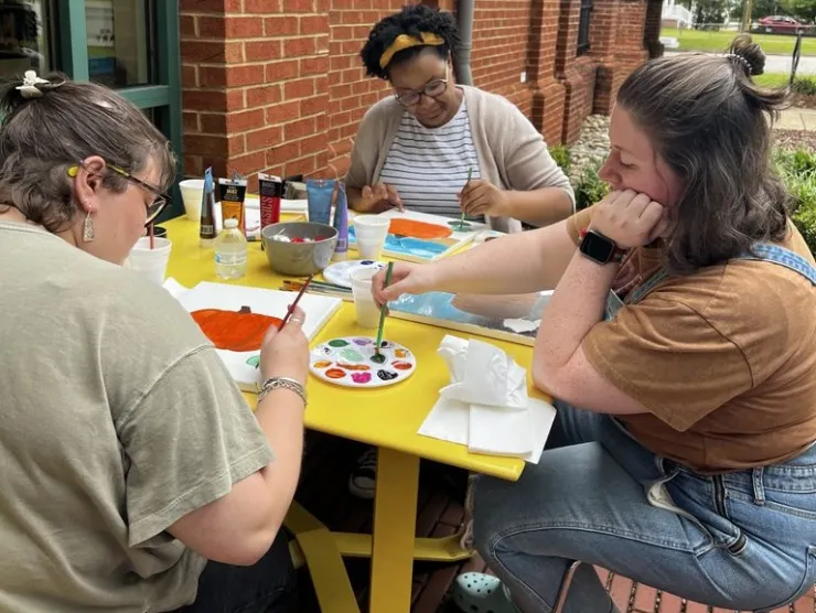 three people painting at a yellow table