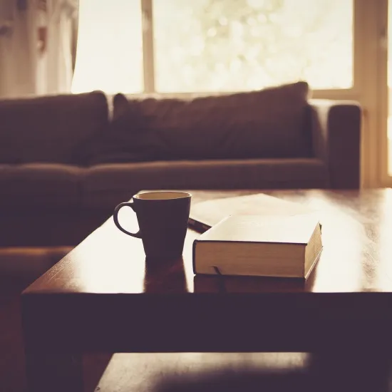 A mug and book on a coffee table with brown couch in background