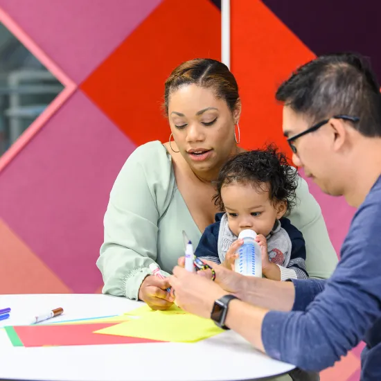 Two adults draw with markers with a toddler
