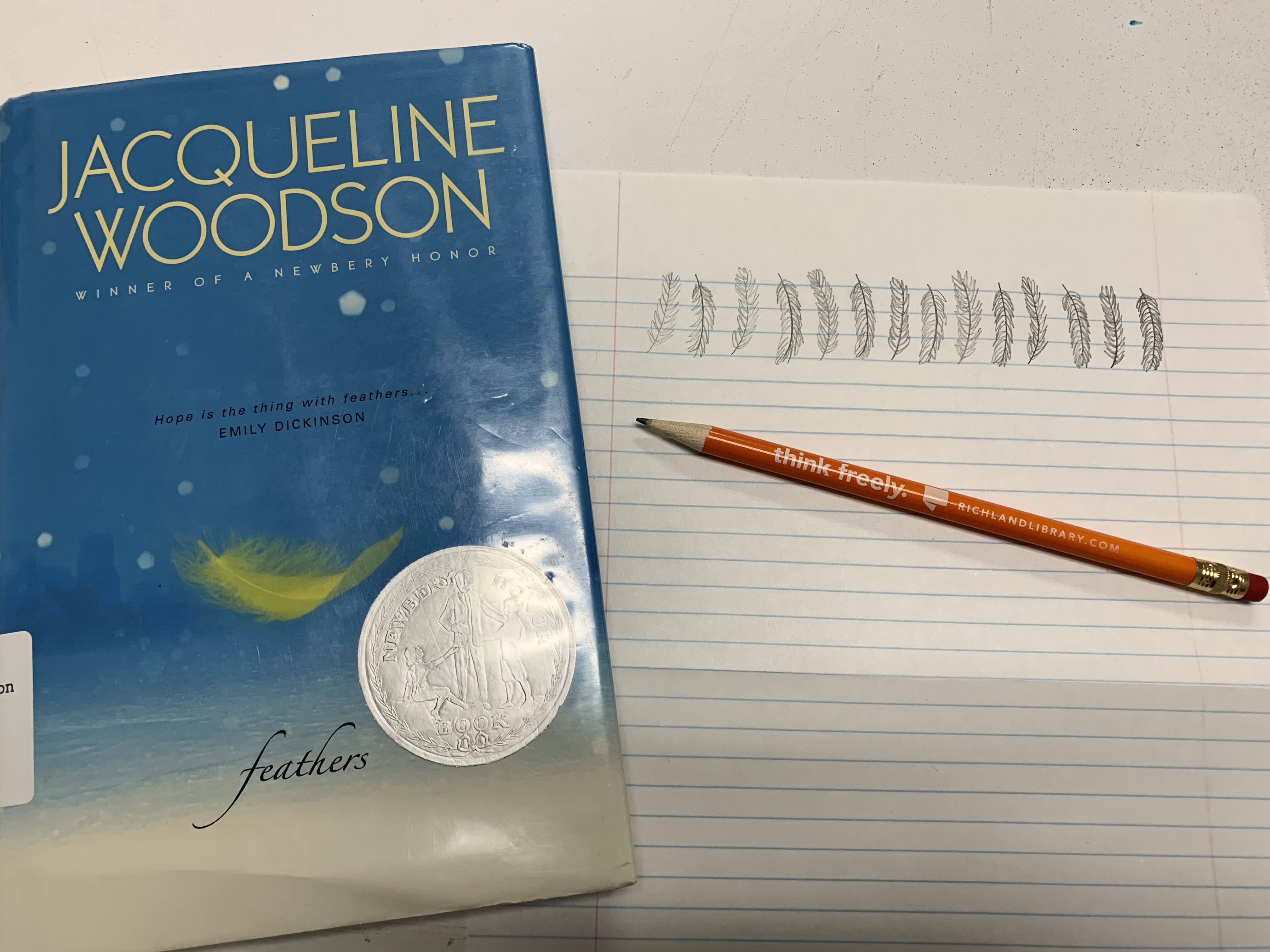 Photo of the book Feathers, by Jaqueline Woodson, next to lined paper with doodled feathers