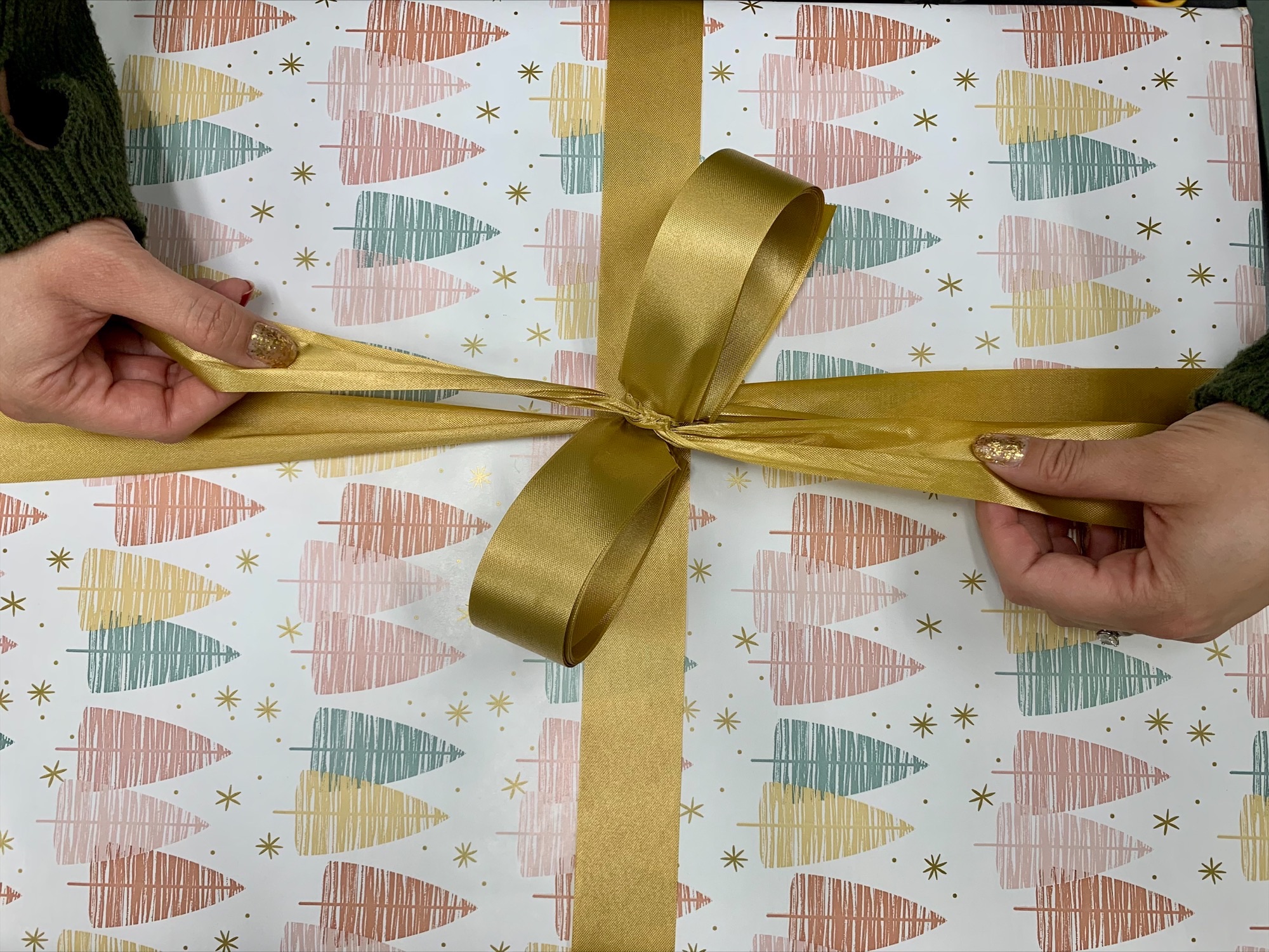 the unfolded gold ribbon loops tied onto the gift box using a double knot