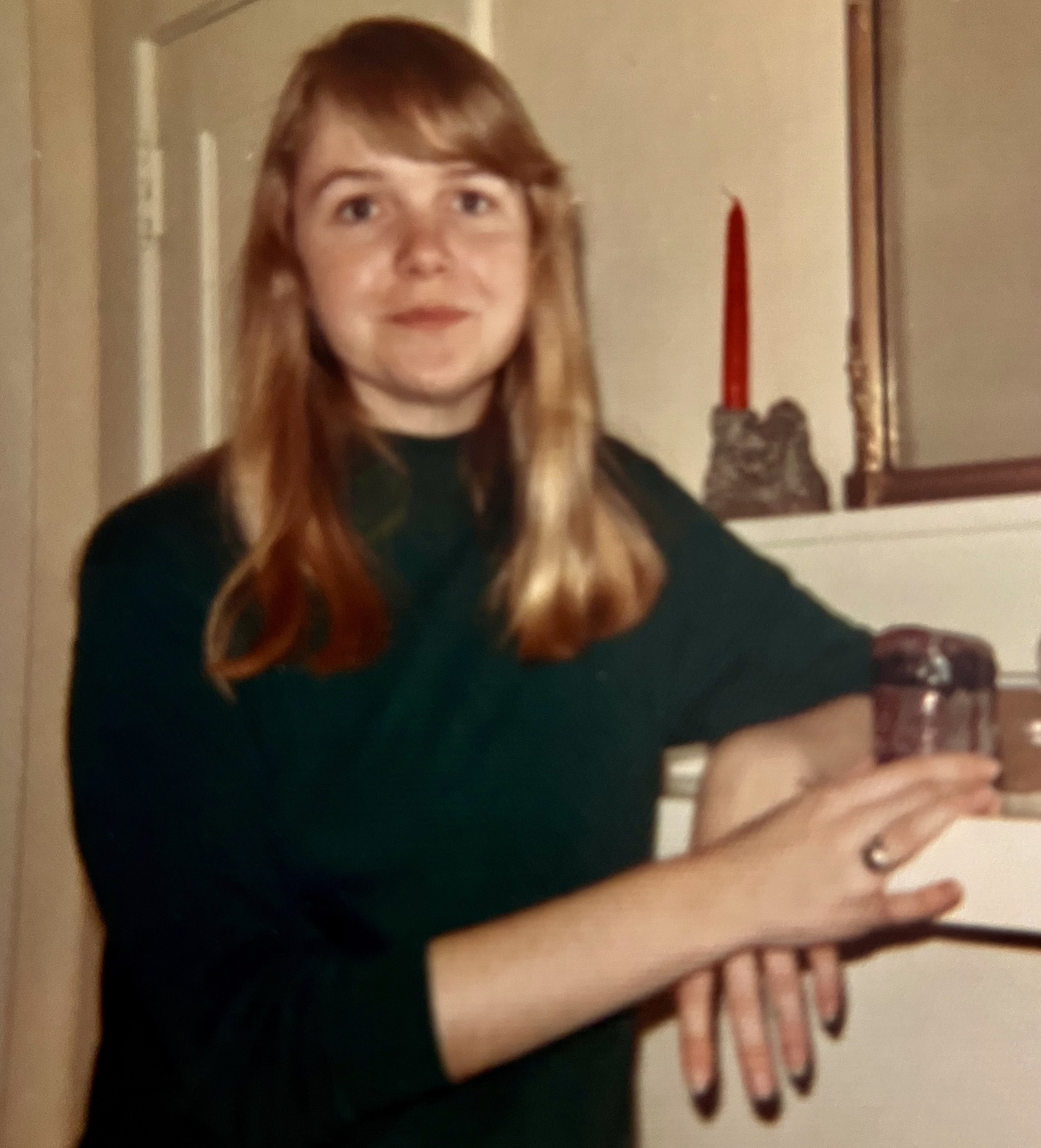 Photo of Jennie Morris. Woman with long blonde hair wearing a black sweater and leaning against a fireplace in the early 1970s