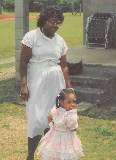 The author of the blog post as a small child, wearing a frilly, pink dress and twirling in front of her mother, who is wearing a long, white skirt and blouse. The two are smiling and playing outside.
