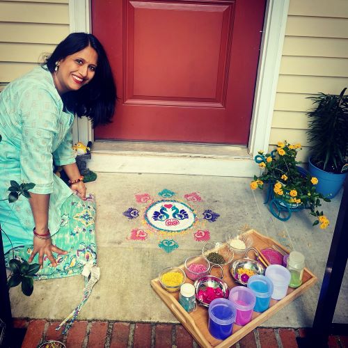 Artist Jugnu Verma poses on front porch with a Rangoli design and her materials
