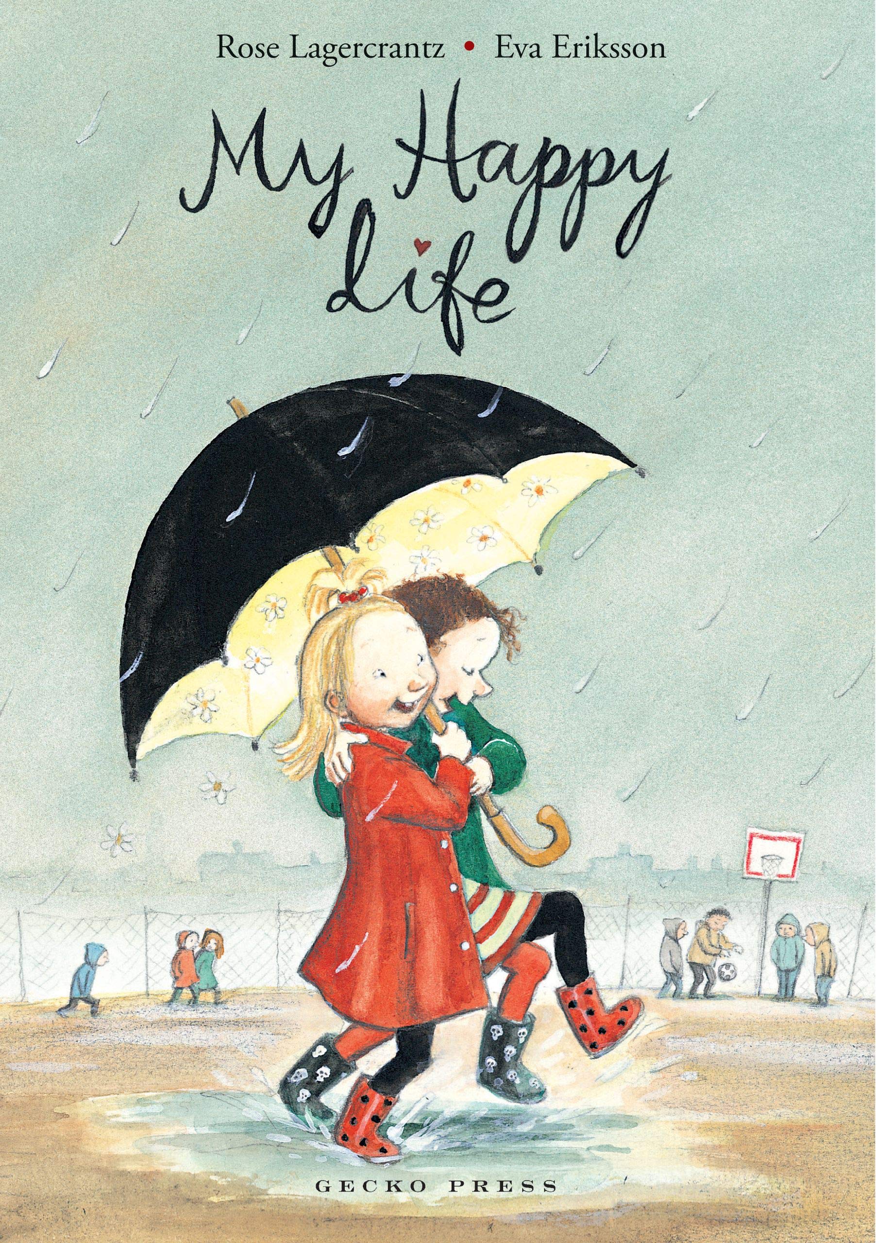 Two young white girls splash in the rain sharing a black umbrella | One girl is blonde wearing a red raincoat | The other girl has dark curly hair and is wearing a green raincoat | Both are laughing and smiling