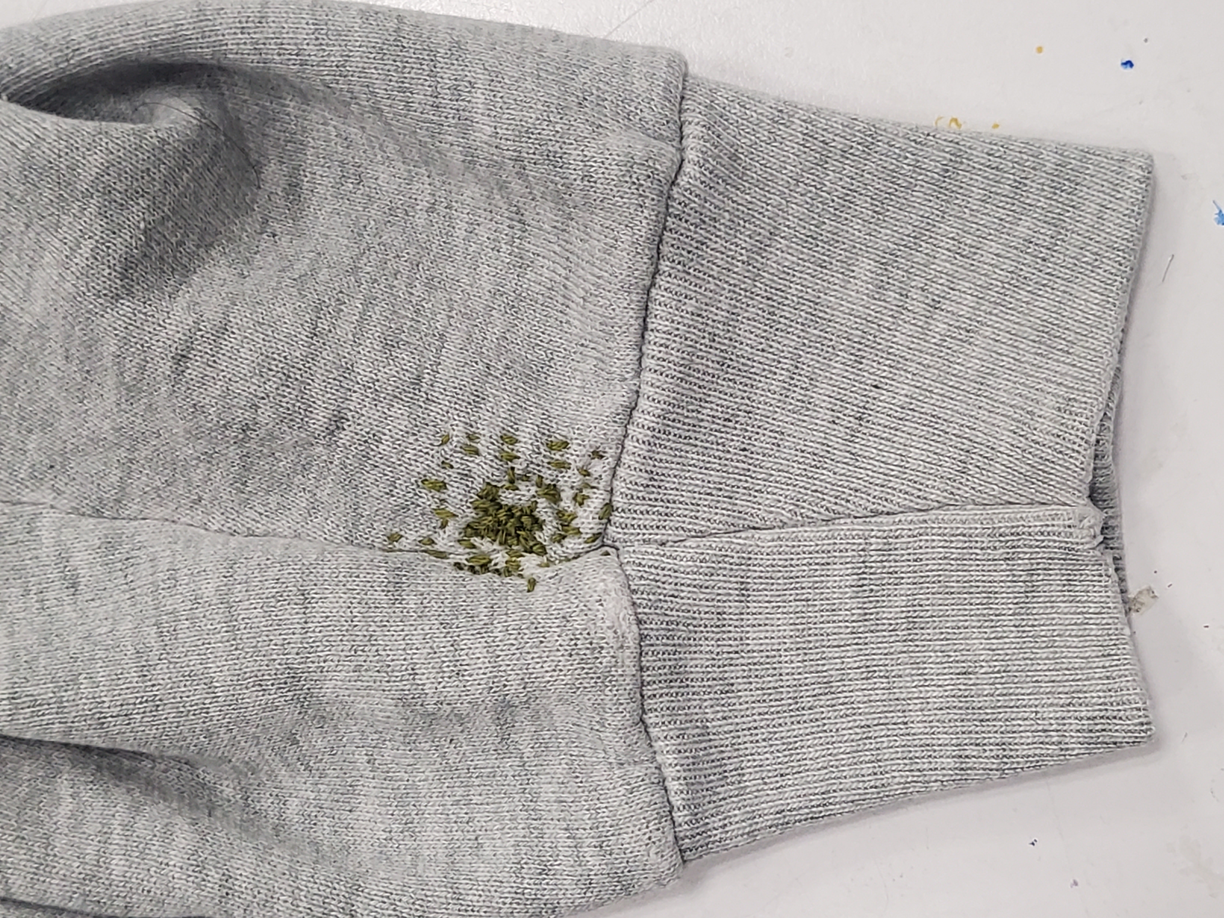 Grey hoodie sleeve with green stitches mended over a hole