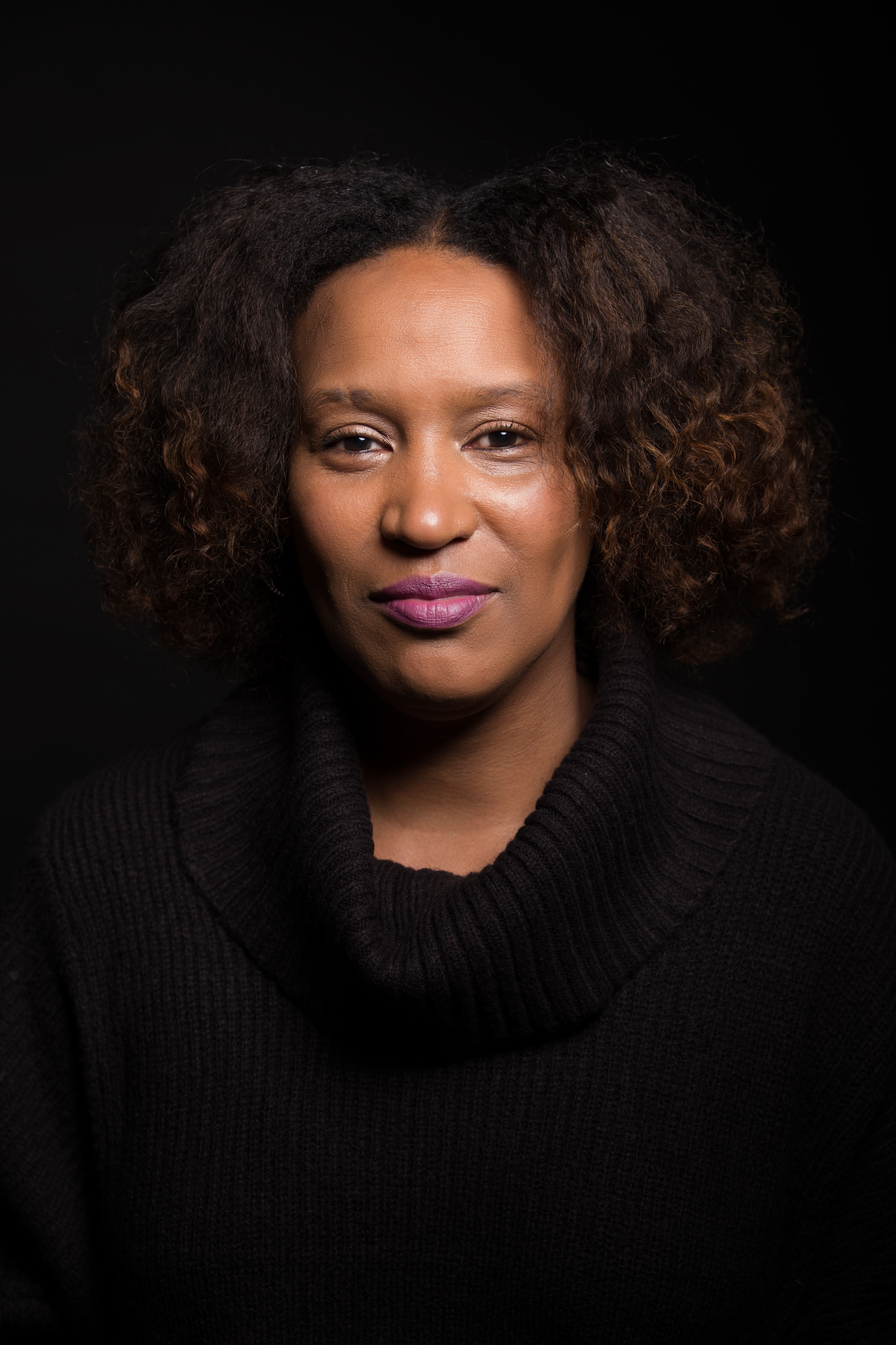 Head shot of Vivian Anderson | A Black woman wearing light purple lipstick and a black turtleneck sweater against a dark background.