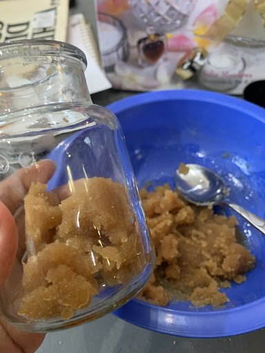 Picture of glass bottle being filled with brown sugar scrub from a blue bowl.