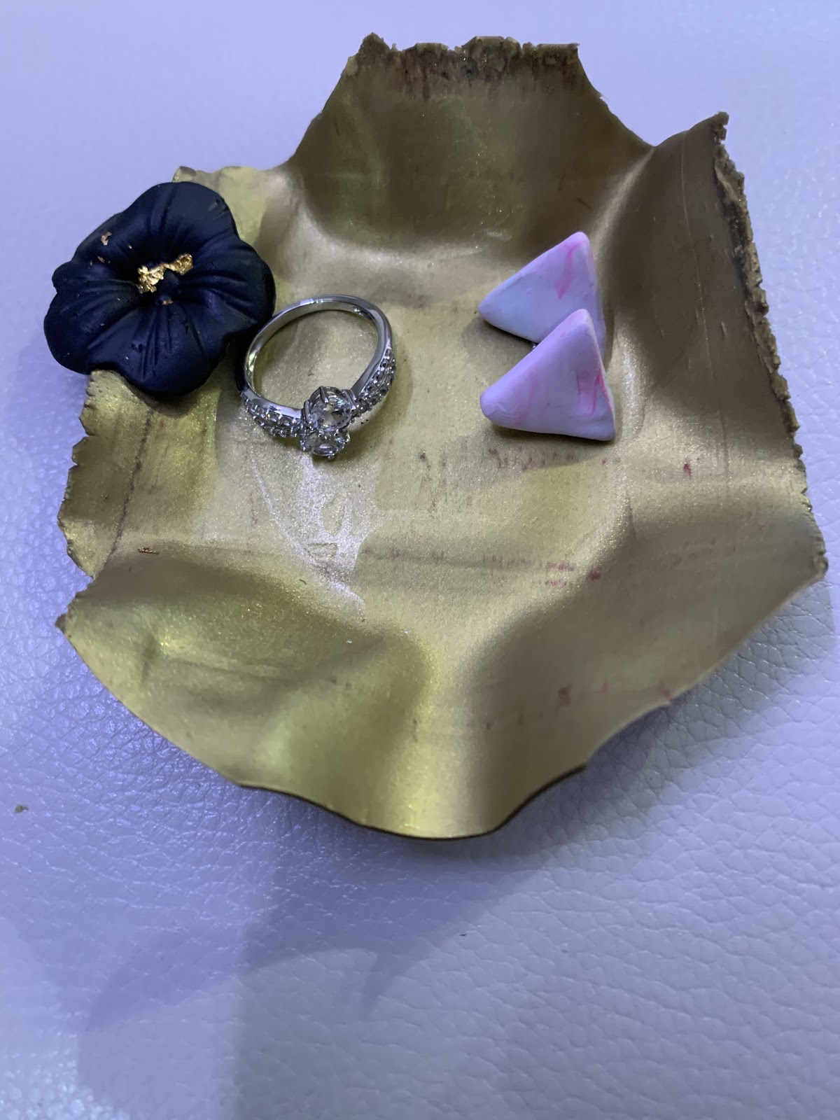 Gold trinket bowl with two lavender colored triangular stud earrings, a diamond wring and a purple daffodil