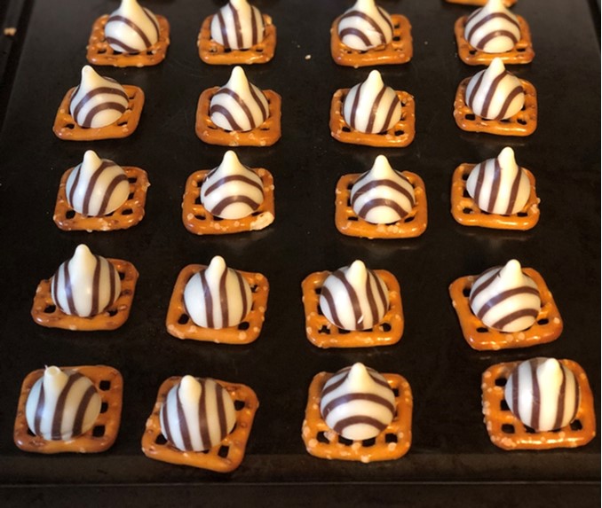 Five rows of four square pretzels with Hershey's Hugs on top of them, on a black background.