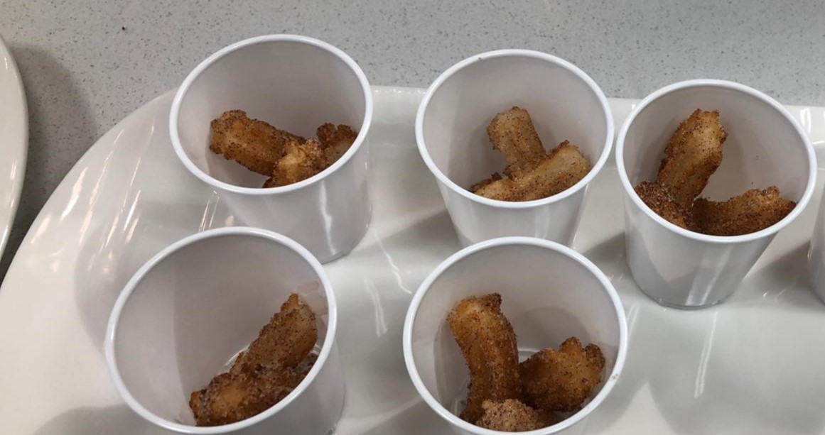 Churros in mini plastic cups, sitting on a white plate.