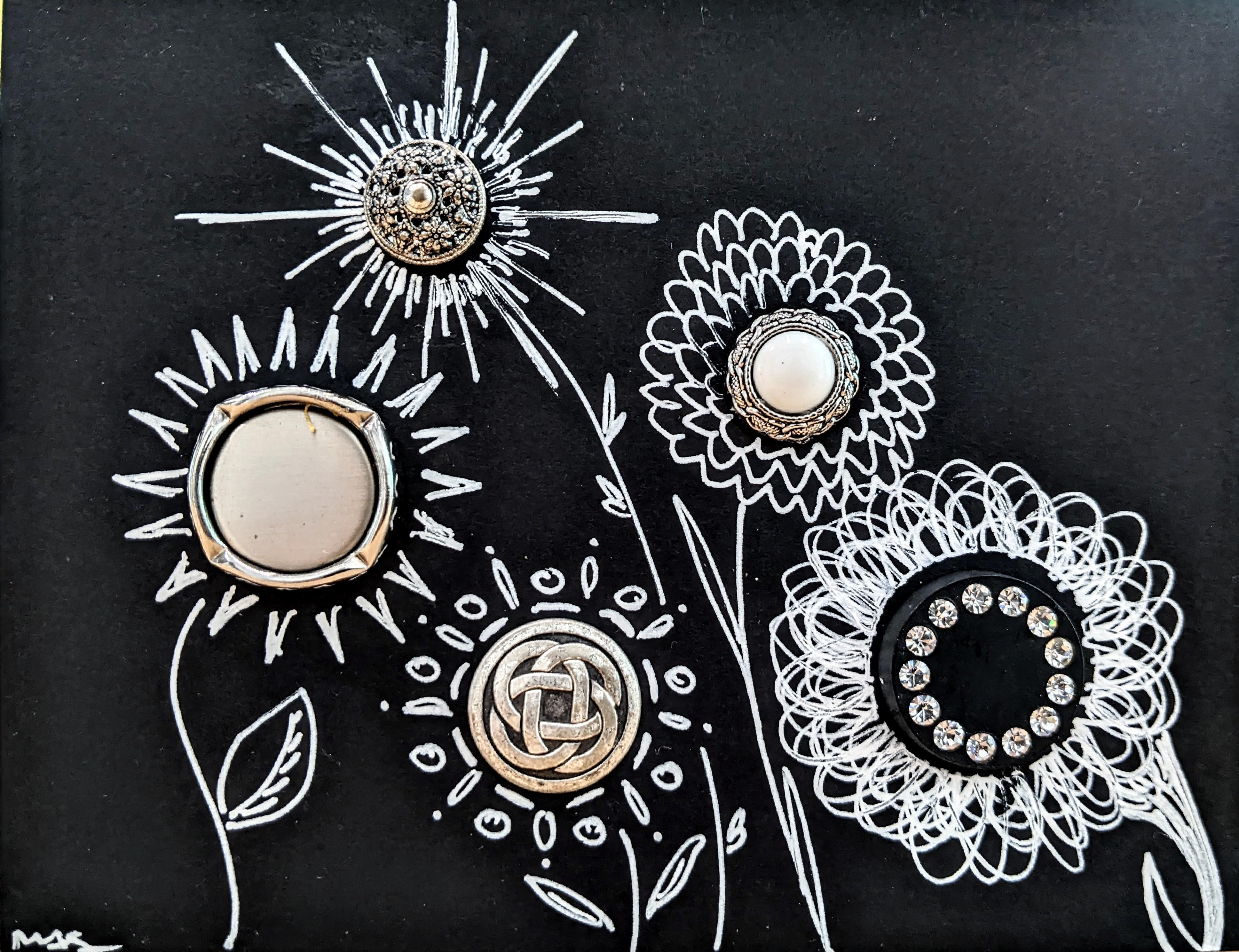 Silver buttons glued to a piece of black cardstock, with floral designs drawn in white pen around each button