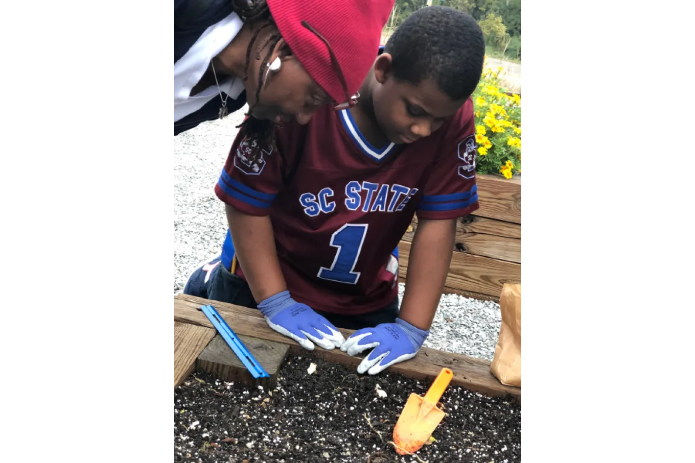 BIPOC teen leans over raised garden bed at Richland Library St. Andrews