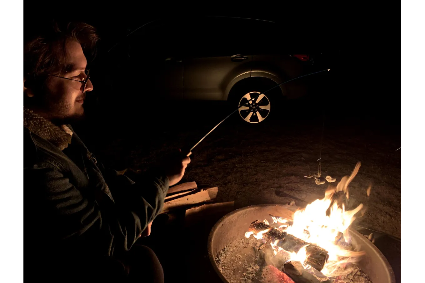 Photo of a man roasting marshmallows over a campfire at night