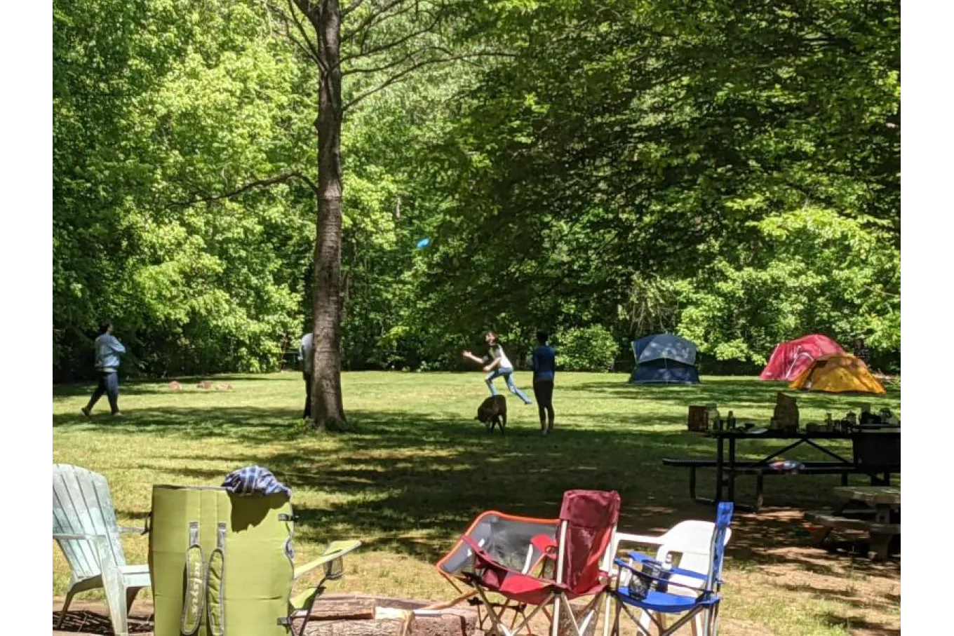 Photo of a campsite with three tents, outdoor chairs, and people playing frisbee.