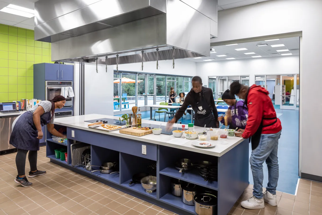 Group of adults cook around the island in the teaching kitchen at Northeast