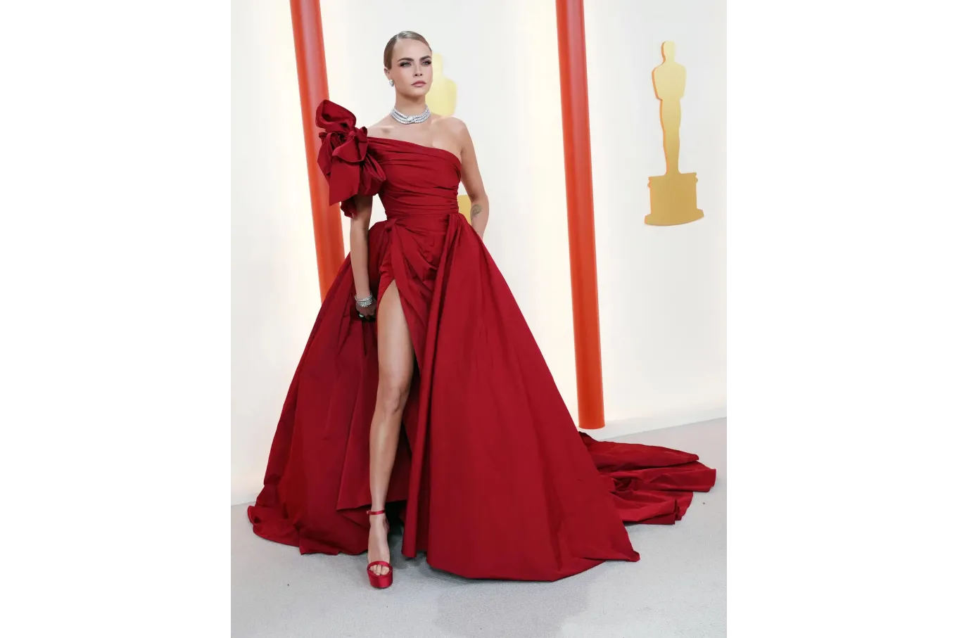 actress Cara Delevingne in a dramatic, deep red dress, with a leg slit and asymmetric sleeve