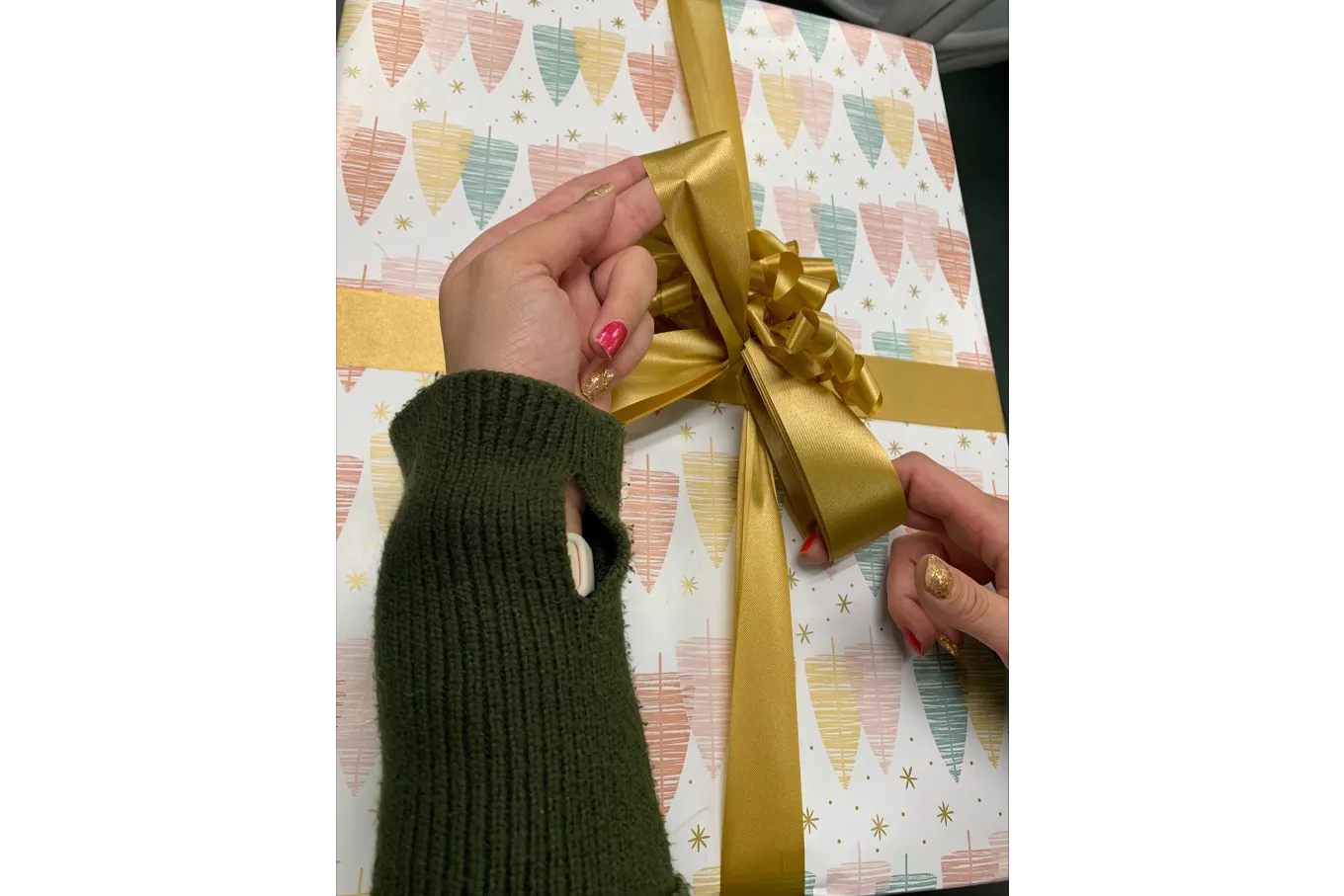 gold ribbon being tied into a bow against a background of multicolored wrapping paper
