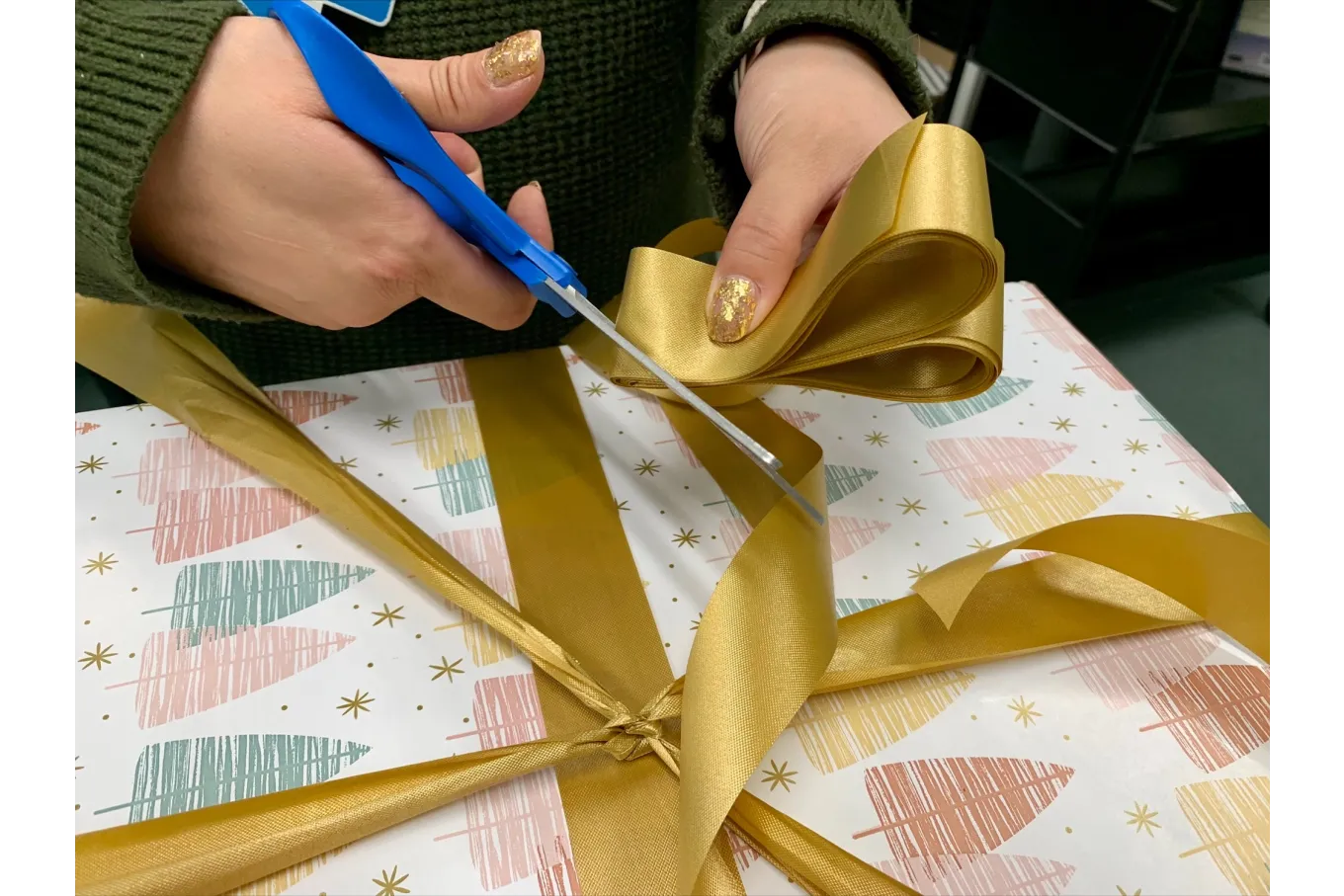 gold ribbon being tied into a bow against a background of multicolored wrapping paper