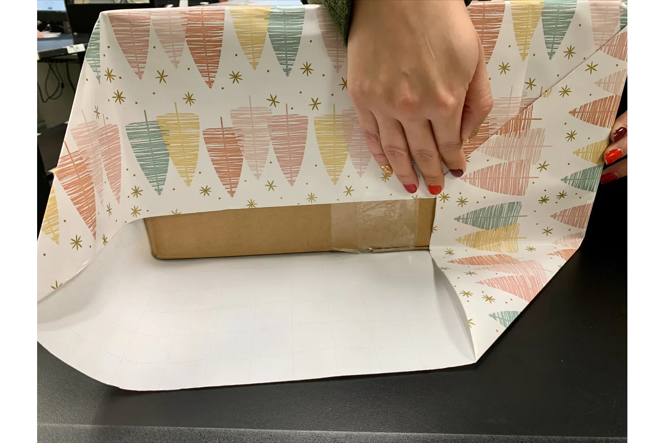 a box being wrapped in multicolored holiday wrapping paper