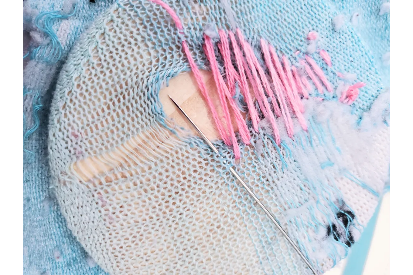 pink thread sewn back and forth over a hole in a blue sock