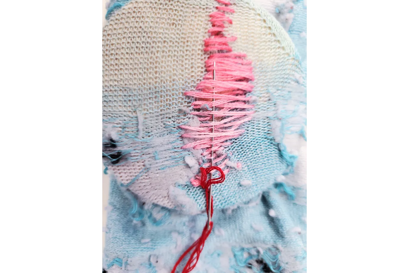 Needle weaves in and out of pink stiches over a blue sock.
