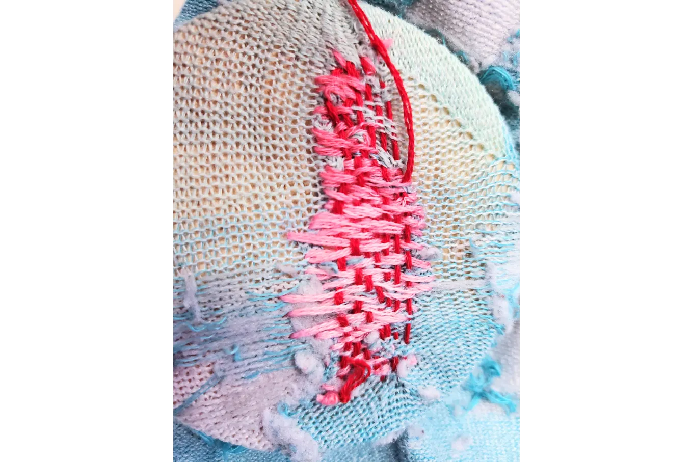 many red threads weave through pink stiches in a blue sock but one group of pink stiches remain