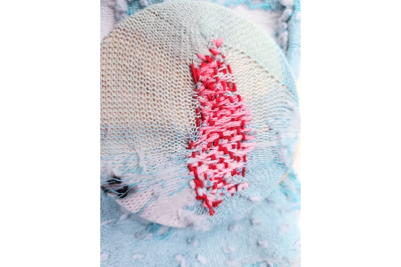 Blue sock with pink and red thread weave covering a hole