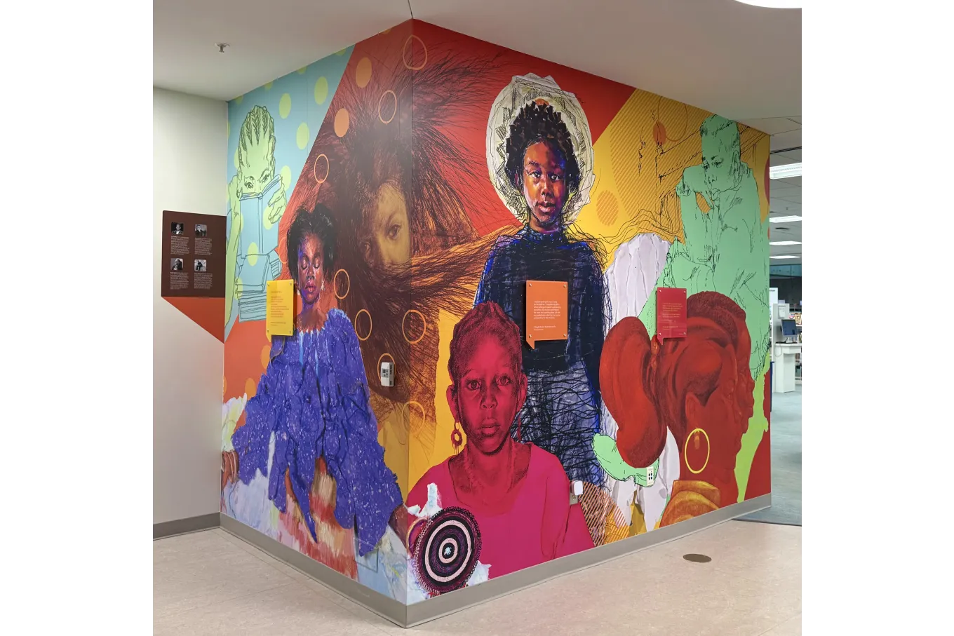 This large corner mural spans two adjoining walls, featuring vibrant, layered portraits of Black children and women against bold red, yellow, green, and blue backgrounds with graphic patterns and circular motifs. Faces range from detailed and painterly to sketched and silhouetted, forming a dynamic collage that celebrates identity and growth. Integrated text panels enhance the design, transforming the library hallway into a vivid, immersive space.