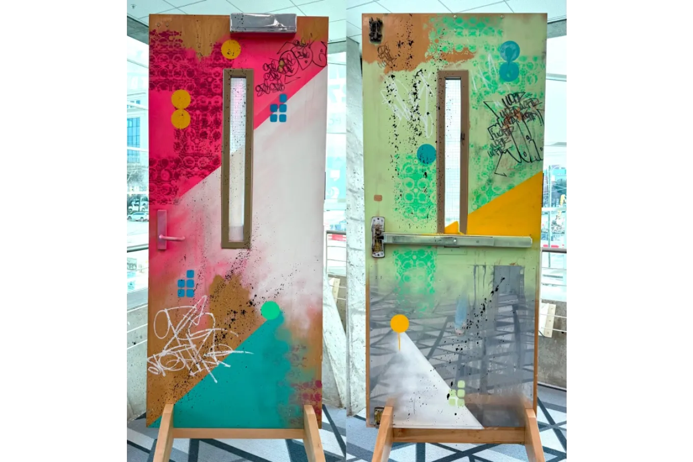 Two views show a freestanding door transformed into a graffiti-inspired art piece, painted on both sides with layered spray paint, stencil patterns, splatters, and graphic shapes. One side features bold pink and coral tones with teal, yellow, and blue accents, while the other blends softer greens, yellow, and gray with similar markings; a narrow vertical window and metal hardware remain visible, and the door stands upright on a wooden support in a modern indoor space.