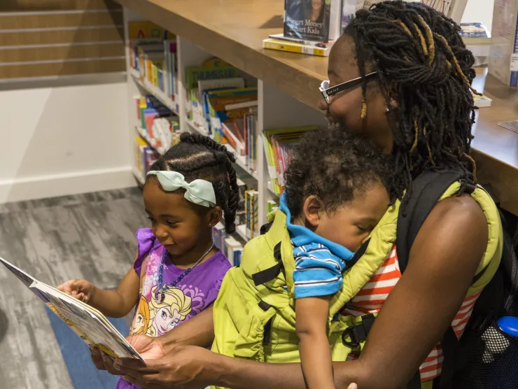Black woman sits on floor with two small children and reads book at Richland Library Ballentine