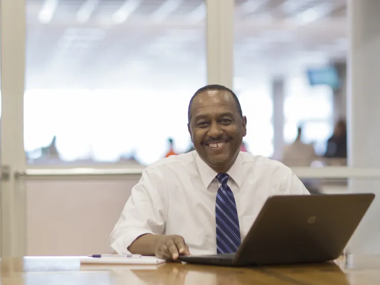 Black male wearing a white shirt and tie sits in front of a lap top computer at Richland Library
