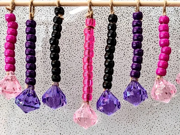 Beaded wall hanging made from pink, purple, and black pony beads with large plastic pink and purple crystals hanging from the bottom