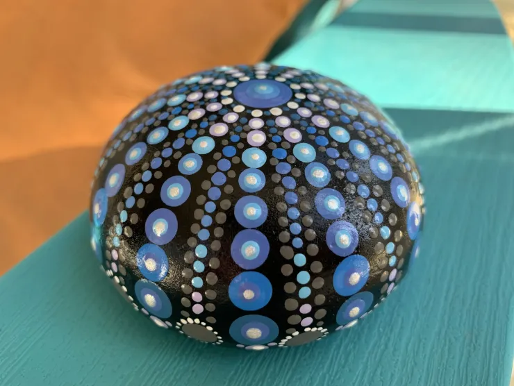 Photo of a round rock, painted black with various shades of different sized blue dots in a repeating pattern on it