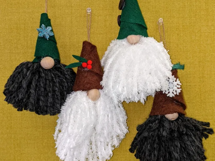 Photo: four winter holiday gnome ornaments. Two gnomes have green felt hats and two have brown felt hats. Two have white beards and two have dark grey beards. Each has a large wooden bead nose. Various embellishments decorate their hats.