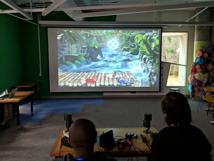 Two teens playing a videogame on a projector screen