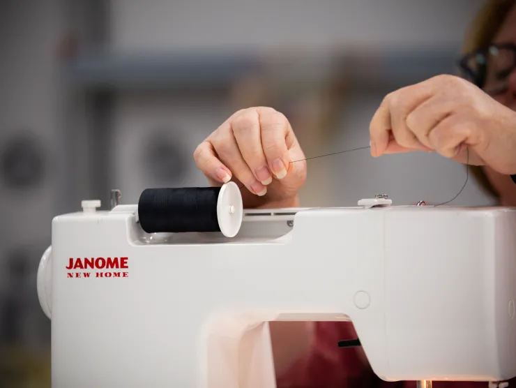 Female customer threads sewing machine. Hands are show above white machine.