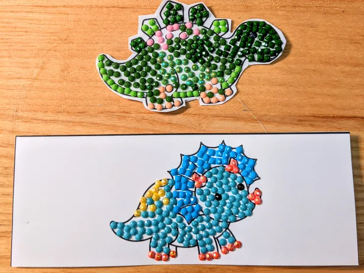 Photo: two chibi dinosaurs (a stego and a triceratops) colored using diamond dots (greens for the stego and blues for the triceratops)