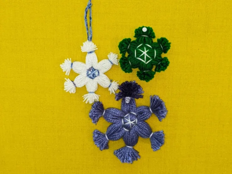 photo: three snowflake ornaments made of yarn: blue, green, and white