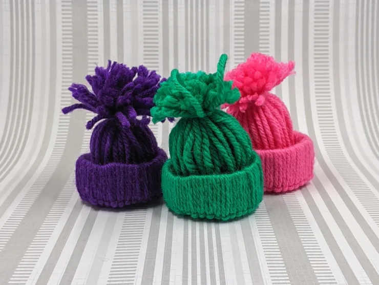 Photo: three winter hat ornaments made of yarn - one pink, one green, one purple
