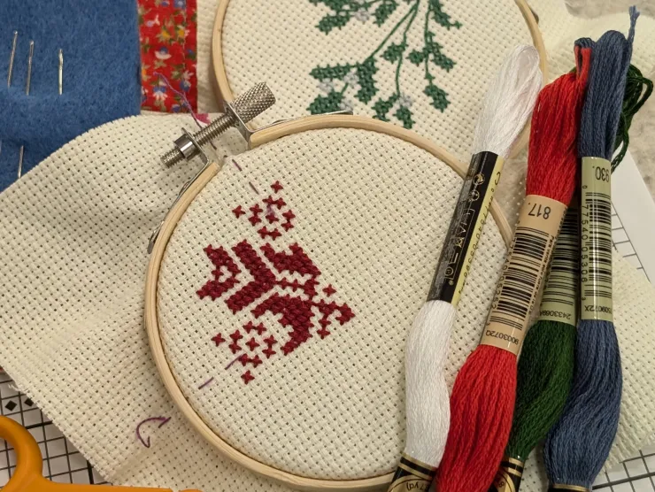 Two small cross stitch embroidery hoops are resting on a gridded pattern, surrounded by embroidery tools and supplies.