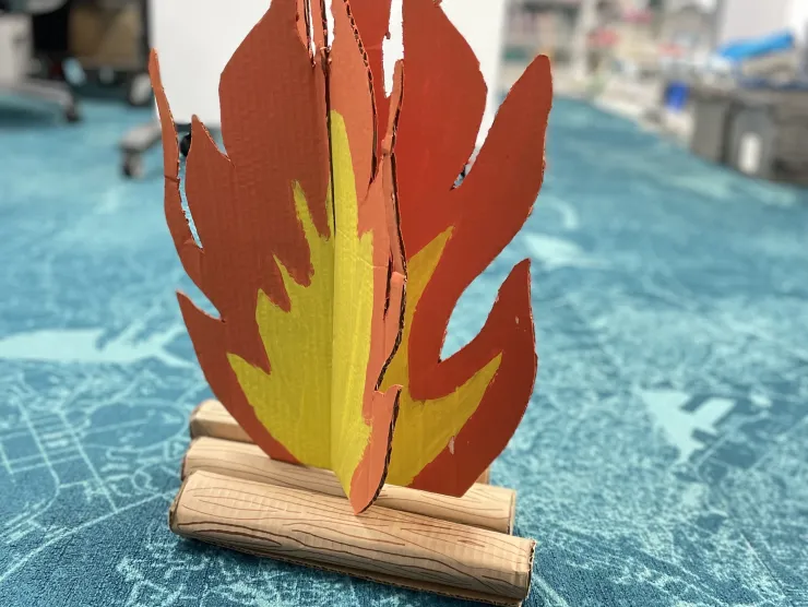 A red and yellow campfire and logs painted onto cardboard.