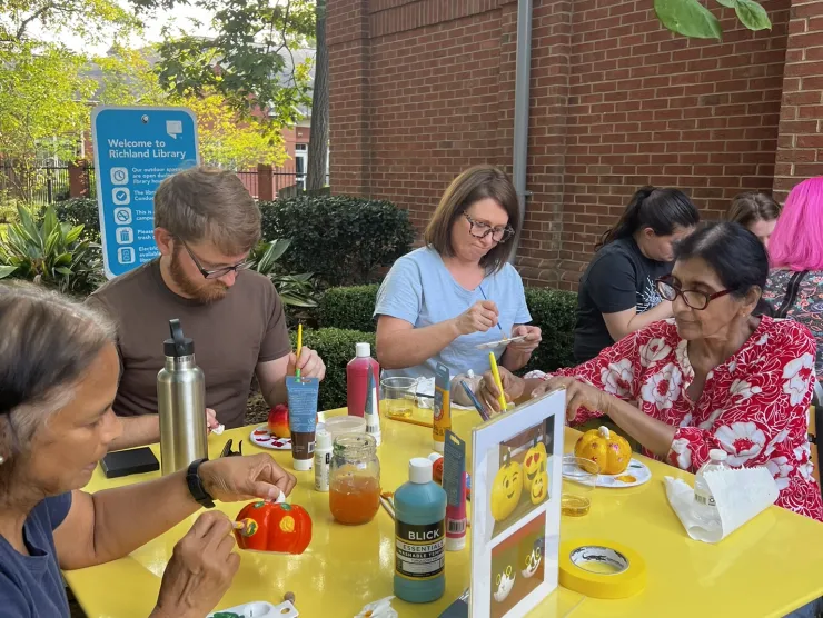 A group of people doing crafts while sitting at a yellow table outside.