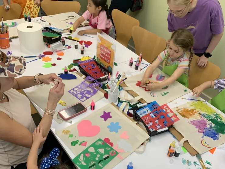 A white table full of various craft materials surrounded by seated children doing crafts. 