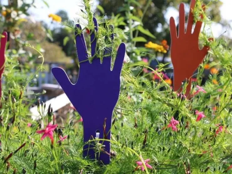 Colorful red and blue hands pop out of a garden bed.  The blue one has a vine wrapped around the fingers.  