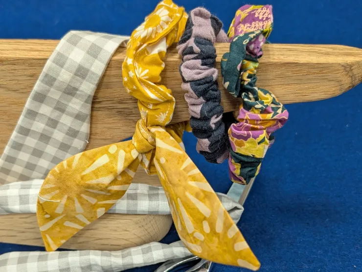Several scrunchies made of different fabrics in different phases of completion on a tailor's clapper.