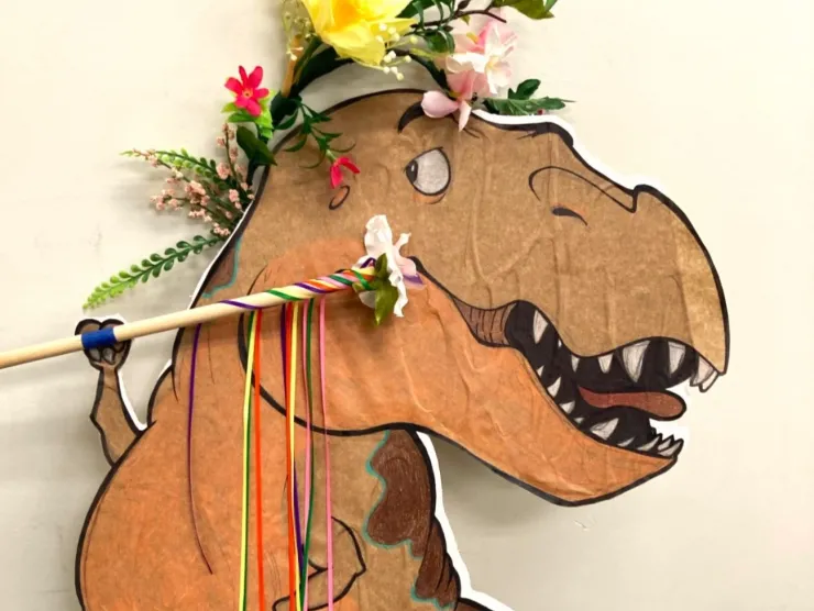 A cartoon dinosaur cutout wearing a flower crown and holding a wand.