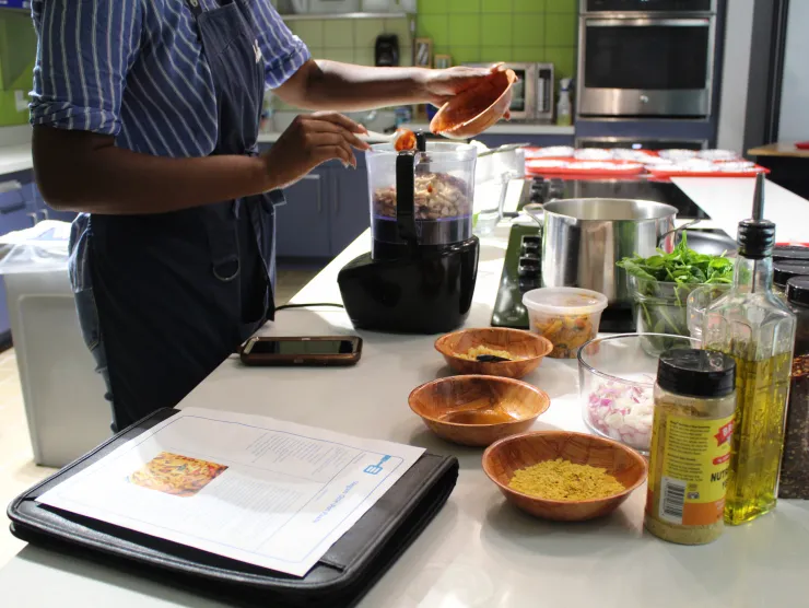 Participant adding ingredients to a food processor with spices and vegetables laid out on the counter.