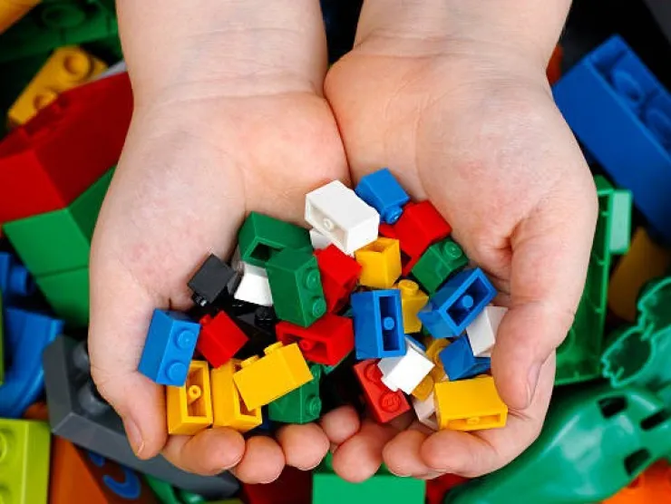 a pair of hands holding multi-colored lego bricks against a background of more multi-colored lego bricks
